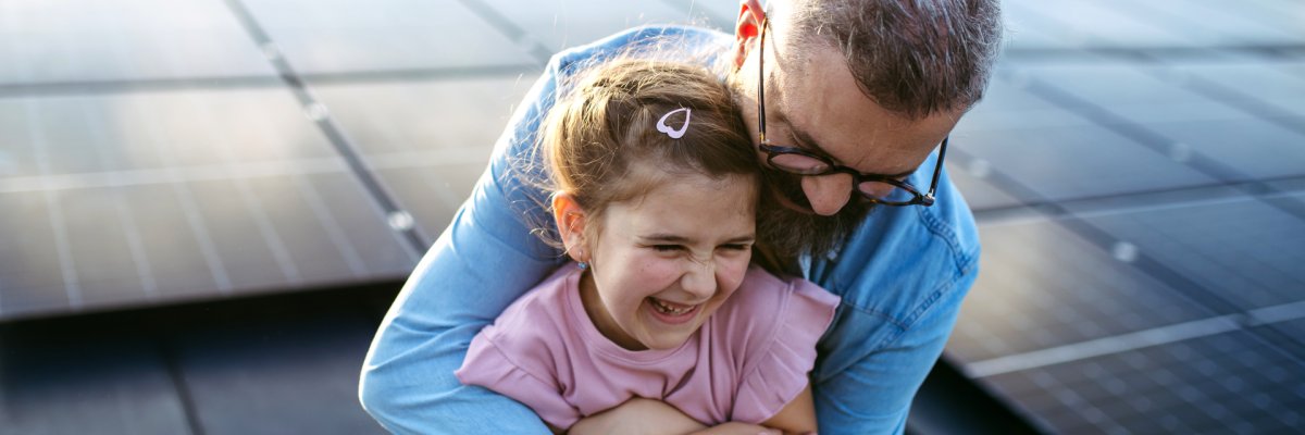 Father with girl on roof with solar panels, hugging. Rooftop solar or photovoltaic system. Sustainable future for next generation. Father with girl on roof with solar panels, hugging. Rooftop solar or photovoltaic system. Sustainable future for next generation.